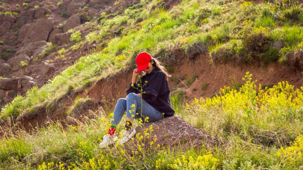 woman in black jacket and blue denim jeans sitting on green grass during daytime